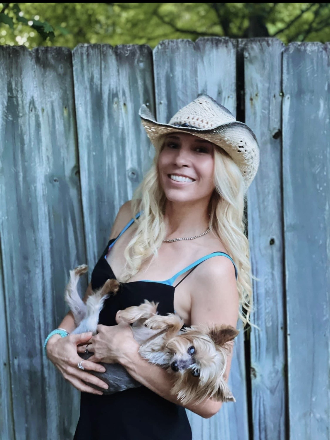 Starr Valdez smiling in a straw cowboy hat, holding her dog Angel